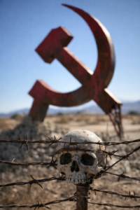 Human skull entangled in barbed wire with blurred hammer and sickle in background