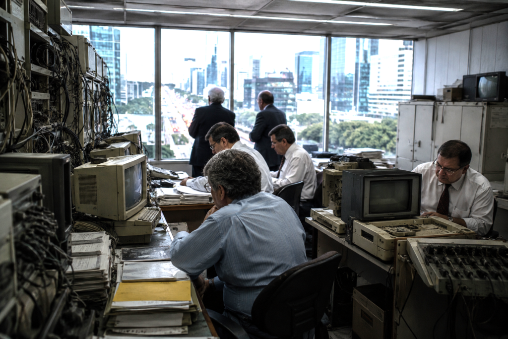 Public officials in an outdated technology room while a modern digital city moves outside.