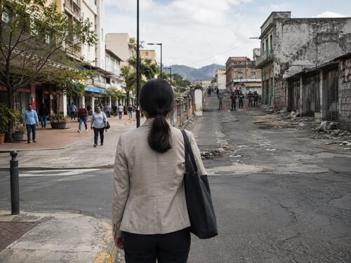 Anonymous professional at a crossroads between an open urban street and a restricted, deteriorated environment.