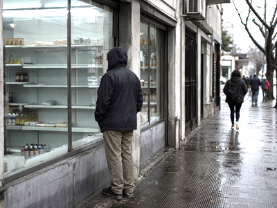 Anonymous citizen looking into a sparsely stocked neighborhood shop on a rainy Montevideo street.