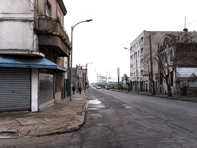 Montevideo urban scene contrasting stagnant local commerce with productive port activity in the distance.