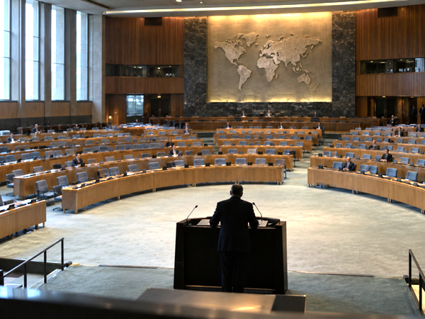 Nearly empty international assembly hall during a formal speech, symbolizing the distance between political rhetoric and public representation.