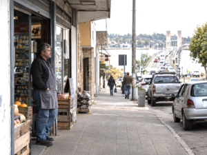 Local shop owner on a quiet commercial street as cars head toward a border crossing in Uruguay.