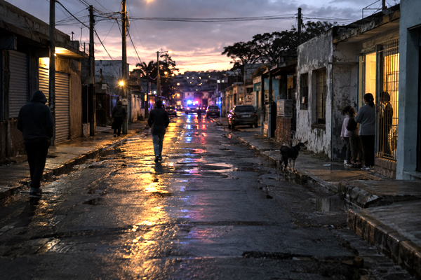 Residents in a working-class Uruguayan neighborhood at dusk amid signs of insecurity and distant police activity.