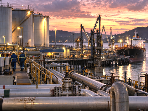 Oil terminal at dusk with workers and industrial infrastructure, symbolizing political pragmatism and shifting ideology in Venezuela.