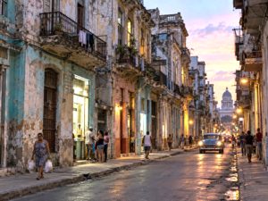 Residents on a deteriorated Havana street amid aging buildings and uneven electrical lighting.